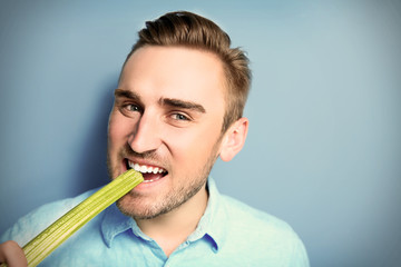 Handsome man eating celery on blue background © Africa Studio