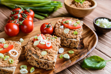 Whole wheat bread slices with sardine spread, tomato and green onion on a wooden background