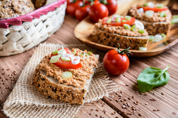 Whole wheat bread slices with sardine spread, tomato and green onion on a wooden background