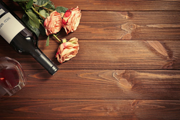 Bottle of wine, glass and roses on a wooden background