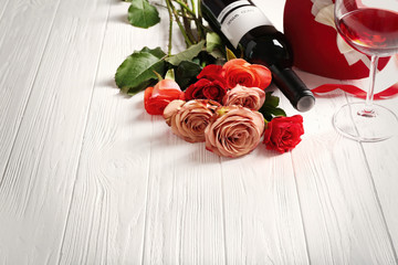 Bottle of wine, box of candies and roses on a wooden background