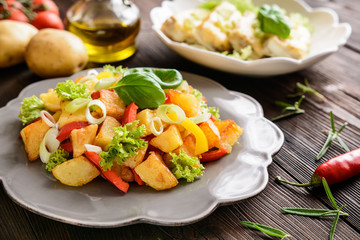 Fried potato salad with lettuce, pepper, onion and baked fish fillets covered with cheese on a wooden background