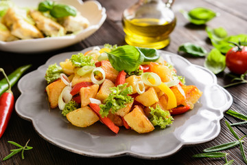 Fried potato salad with lettuce, pepper, onion and baked fish fillets covered with cheese on a wooden background