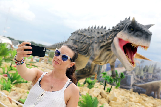 Girl makes a selfie against the background of the layout dinosaur