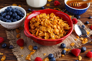 Corn Flakes with berries raspberries, blueberries, glass of milk, and sweet honey.