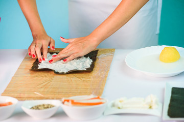 Obraz na płótnie Canvas Hands of woman chef filling japanese sushi rolls with rice on a nori seaweed sheet.