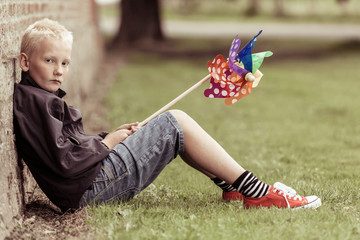 Sad blond boy sits against wall holding whirligig