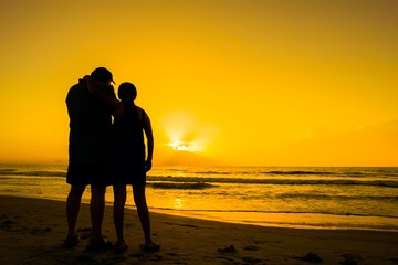 Silhouette of couple with yellow golden sky sunrise at the beach