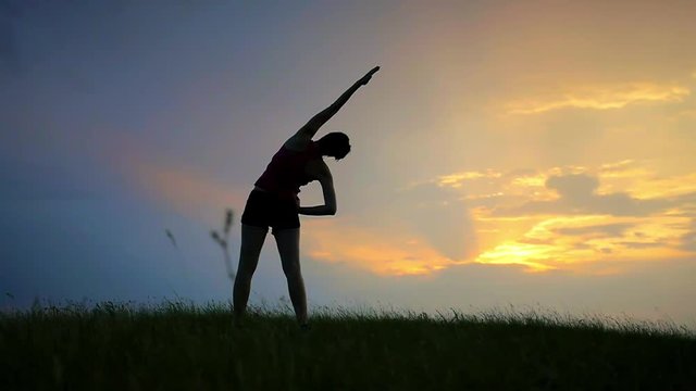 athlete doing exercises on a sunset silhouette of a girl