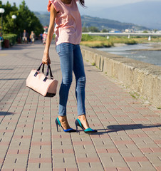 Girl in pink blouse and blue jeans with handbag walking on embankment.