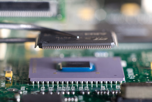 Close up on tweezers holding chip on computer circuit board