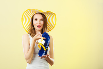 Woman in big yellow summer hat holds flip flops