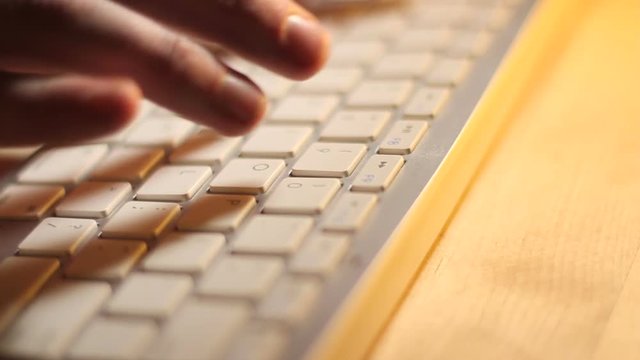 White Keyboard Typing Side View. The camera trucks along a close up of fingers typing on a white computer keyboard.