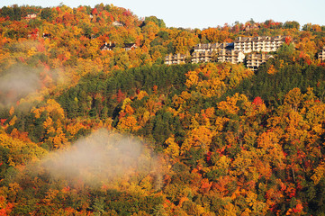 autumn mountain forest in morning sunlight with cloud and hotel buildings