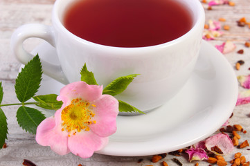 Cup of tea with wild rose flower on old rustic wooden background
