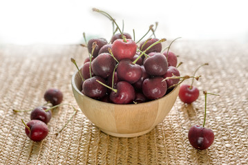 Cherries with water drops in wooden bowl on natural weaving
