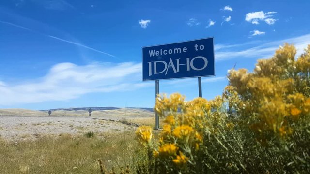 Welcome To Idaho Sign, Wide. Wide angle static shot of a blue "Welcome To Idaho" sign placed along the highway.