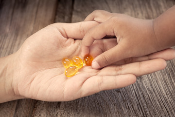 child picks Cod liver oil omega 3 gel capsules on her mother hand
