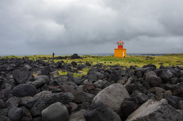 Fototapeta na wymiar Orange lighthouse on the black rock cliff of western Icelandic coast, Snaefellsnes Peninsulain, Iceland