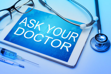 Ask your doctor word on tablet screen with medical equipment on background.