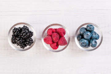 Assorted berries in glass bowls: blueberry, BlackBerry, raspberry on wooden table with text space