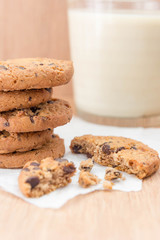 Chocolate chip cookies and a glass of milk on a wooden background.