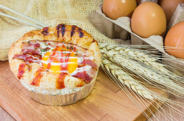 Baked sandwich with egg, cheese and ham. Hot breakfast. Bun with liquid egg, ham and melted cheese on natural wooden background.