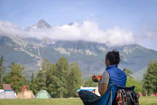 Young woman enjoying view of dramatic mountains while having breakfast in a camp. Selective focus. High Tatras, Slovakia.