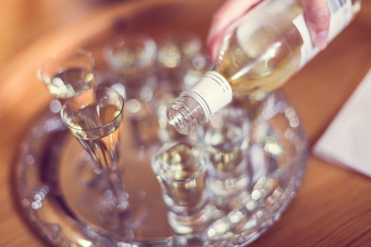 Closeup of hand of person pouring snaps (schnaps alcohol) into small glasses on traditional Swedish Midsummer celebration in June.