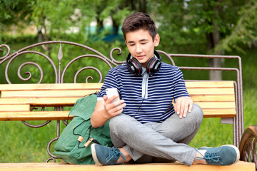 Obraz premium Asian teenager sitting on a bench with a school backpack, cell p