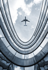 Modern architecture building with flying airplane in background. Low angle view blue colorized picture