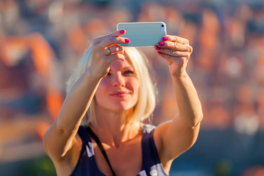 Female traveller make a selfy photo against the background of the old city of Dubrovnik from the mountain to her phone for Instagram or other social networks. Travel to Croatia. Summer vacation.