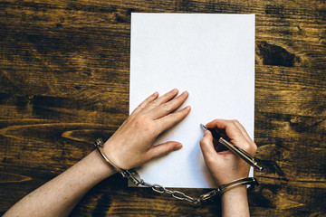 Female hands cuffed signing confession, top view