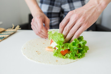 man prepares to roll fast food.
chicken nuggets, lettuce, tomato, cheese, Mexican tortillas