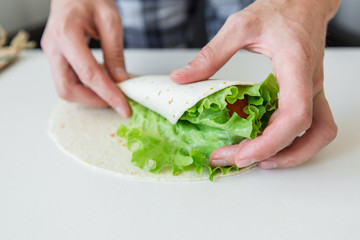 man prepares to roll fast food.
chicken nuggets, lettuce, tomato, cheese, Mexican tortillas