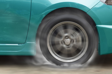 Green car racing spinning wheel burns rubber on floor.