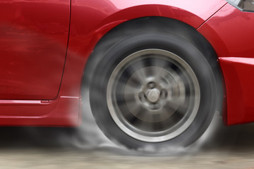 Fototapeta na wymiar Red car racing spinning wheel burns rubber on floor.