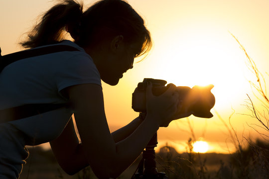 silhouette portrait of a young woman photographing a beautiful nature at sunset on photo equipment - Powered by Adobe