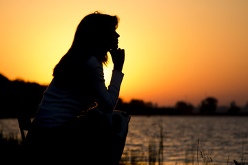 silhouette portrait of a beautiful young woman sitting on a chair by the river at dawn
