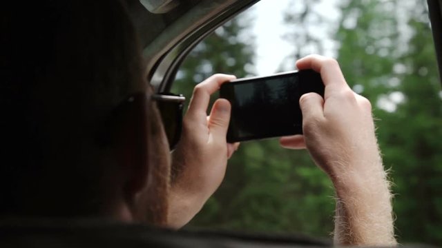 Back view of young couple driving in car and taking photos of road with smartphone