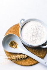 Whole flour in bowl with wheat ears on white background
