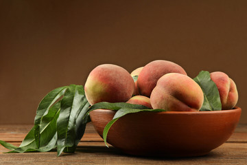 Ripe peaches with leaves in bowl on a brown wooden background