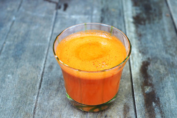 A glass of carrot juice on a wooden table.