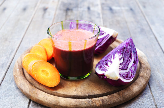 A Glass Of Mixed Carrot And Purple Cabbage Juice On A Wooden Cutting Board.