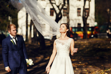 Naklejka premium Wind blows a delicate bride's veil up while she stands with a gr