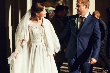 Fototapeta premium Bride and groom walk along the street in the sunrays holding eac