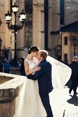 Wind blows a veil around newlyweds while they kiss on the old sq