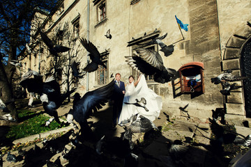Bride and groom stand behind the flying pigeons