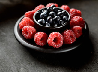 raspberries and blueberries in a bowl on a dark background