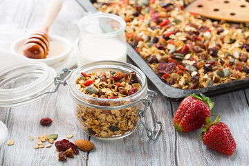 Fresh granola, muesli with berries, honey in a glass jars on a white wooden background, selective focus
